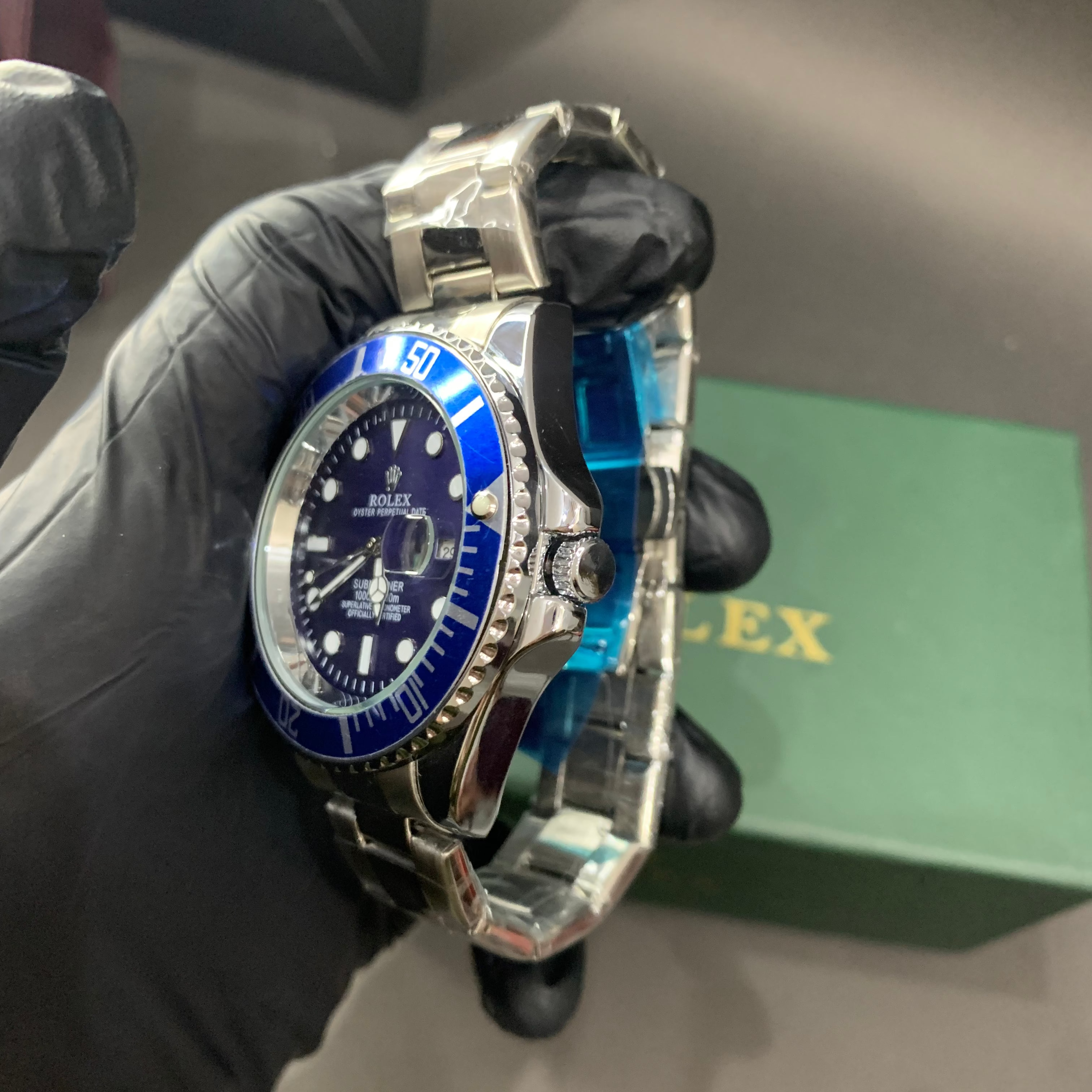 Rolex watch held by a gloved hand with a green box in the background